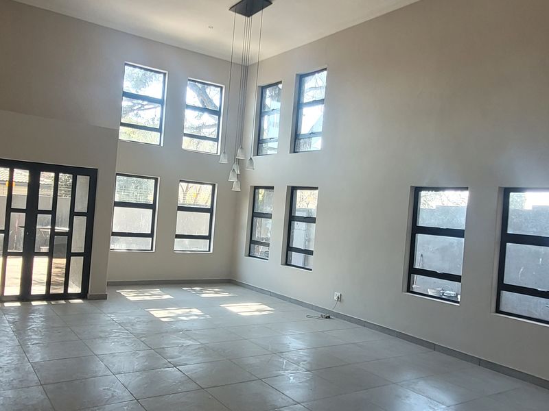 Spacious, light-filled living area featuring double volume ceilings, large aluminium-framed windows, and neutral tiled flooring, offering a versatile open-plan layout.