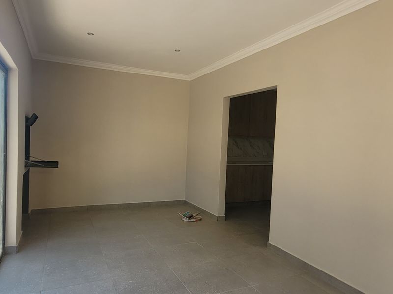 An empty open-plan living area featuring tiled floors, recessed lighting, and a built-in braai, with sliding doors leading to an outdoor space.