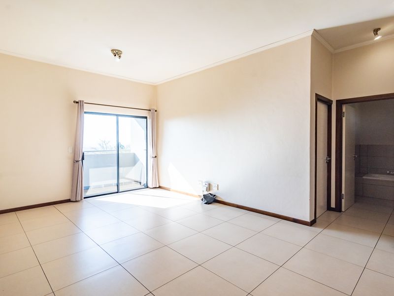 Spacious, light-filled living area featuring neutral tiled flooring, sliding glass doors leading to a balcony, and direct access to an adjoining bathroom.