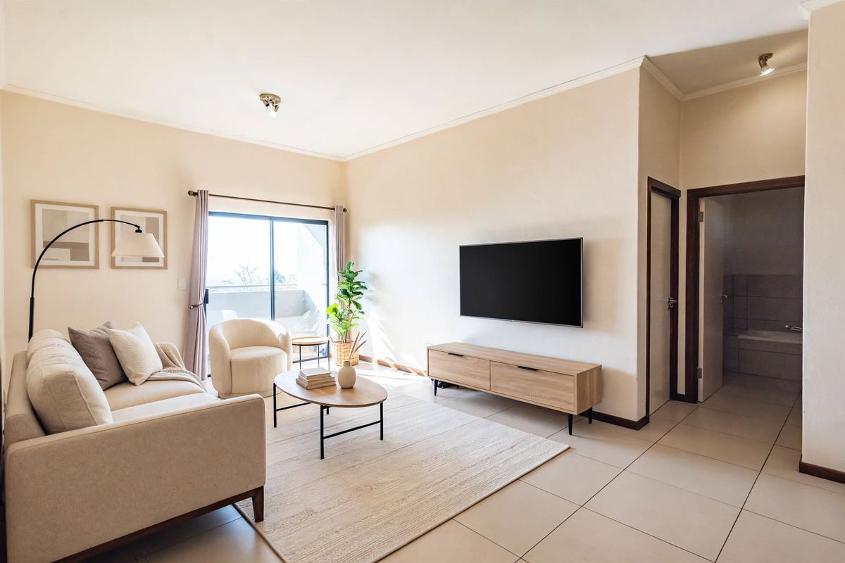 A bright and well-maintained living room featuring neutral tiled flooring, coving, and a sliding glass door providing access to an outdoor area.