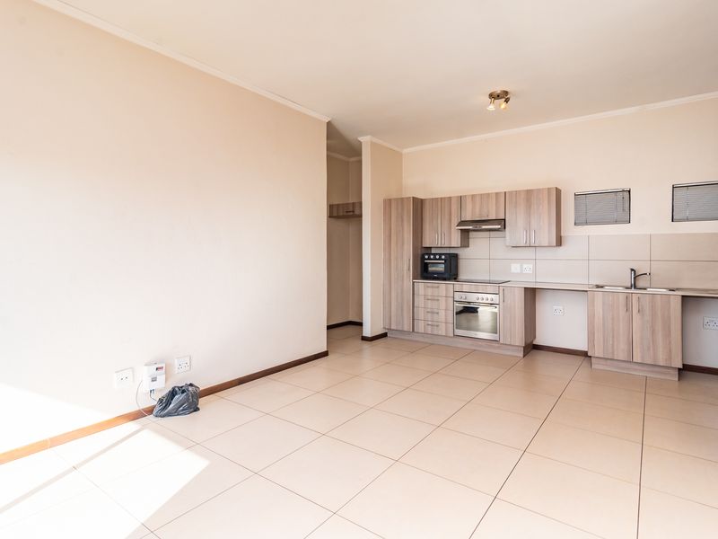 An open-plan kitchen and living area featuring neutral tiled flooring, modern wood-finish cabinetry, and integrated cooking appliances in a clean, vacant space.