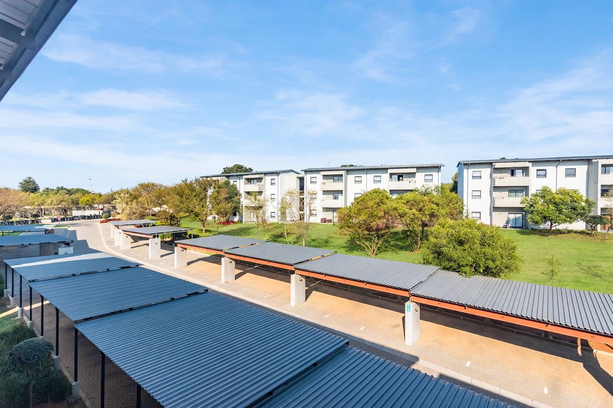 An elevated view of the apartment complex grounds, featuring covered parking bays, paved driveways, and well-maintained communal garden areas between the residential buildings.