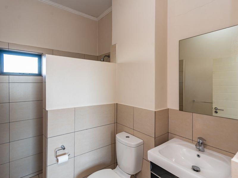 A functional bathroom featuring a shower, toilet, and vanity basin with a wall-mounted mirror and neutral tiled finishes.