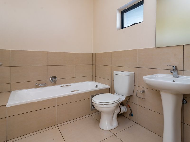 A functional bathroom featuring a built-in bathtub, pedestal basin, and toilet, finished with neutral wall and floor tiles.