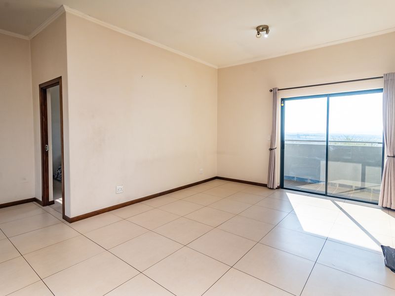An empty, sunlit living room featuring neutral tiled flooring and a large sliding glass door providing access to an outdoor balcony.