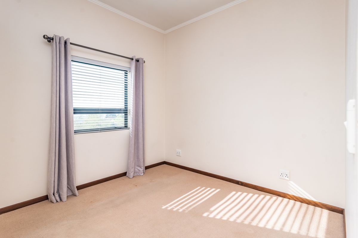 A clean, empty bedroom featuring neutral walls, carpeted flooring, and a window fitted with blinds and curtains.