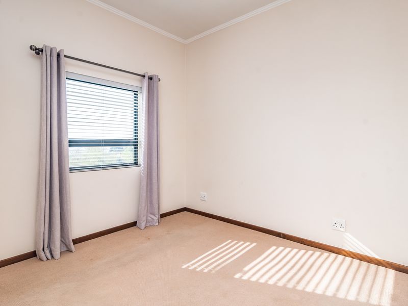 A clean, empty bedroom featuring neutral walls, carpeted flooring, and a window fitted with blinds and curtains.
