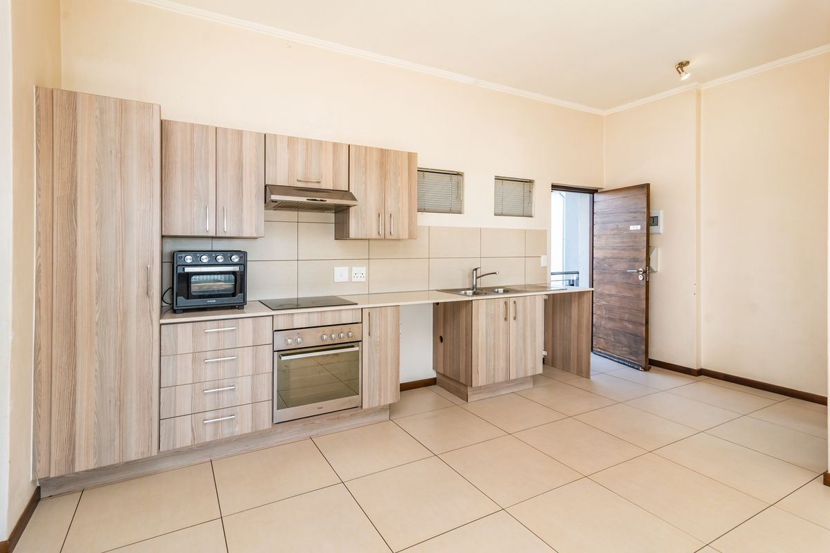 A clean, modern kitchen featuring light wood-finish cabinetry, integrated appliances, tiled flooring, and a neutral backsplash, offering a functional and well-maintained cooking space.