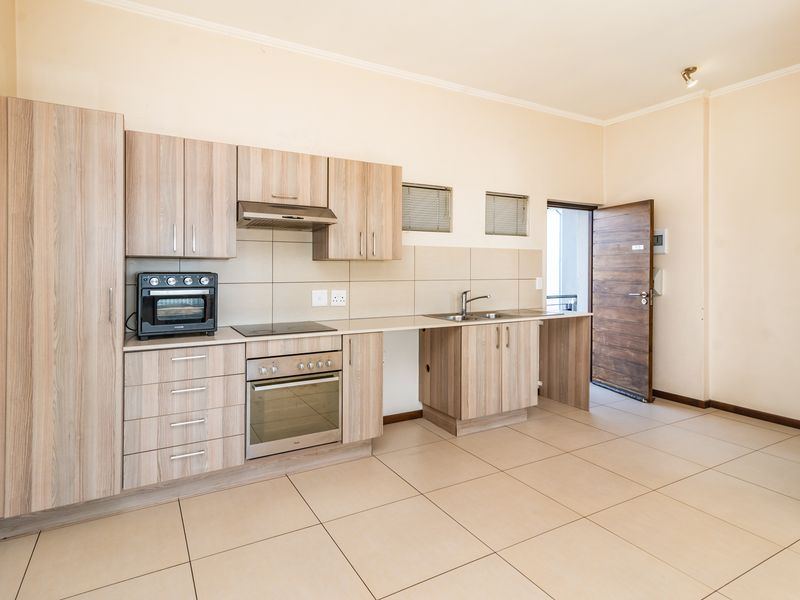 A clean, modern kitchen featuring light wood-finish cabinetry, integrated appliances, tiled flooring, and a neutral backsplash, offering a functional and well-maintained cooking space.