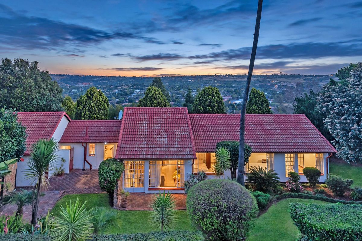 Rear view of the residence featuring a terracotta tiled roof, paved patio area, and established garden overlooking a scenic landscape at dusk.