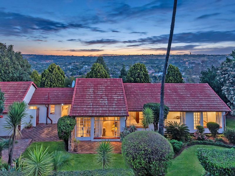 Rear view of the residence featuring a terracotta tiled roof, paved patio area, and established garden overlooking a scenic landscape at dusk.
