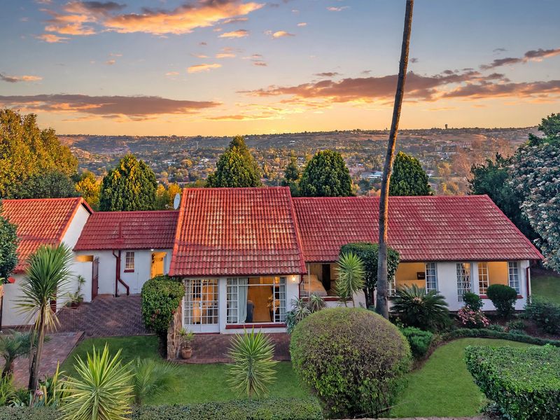 Rear view of the property featuring a tiled roof, paved patio area, and well-maintained garden with expansive sunset views over the surrounding landscape.