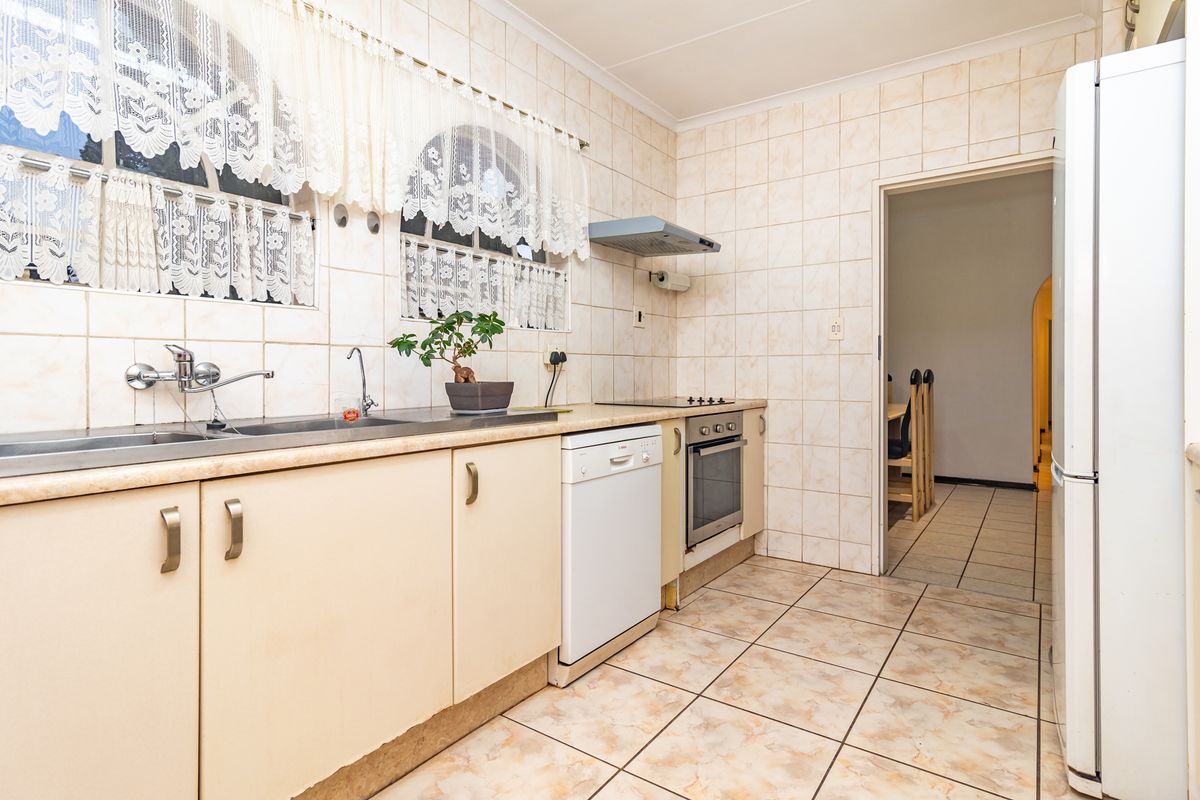 A functional kitchen featuring built-in cabinetry, a stainless steel sink, integrated oven, and hob, finished with tiled walls and flooring throughout.