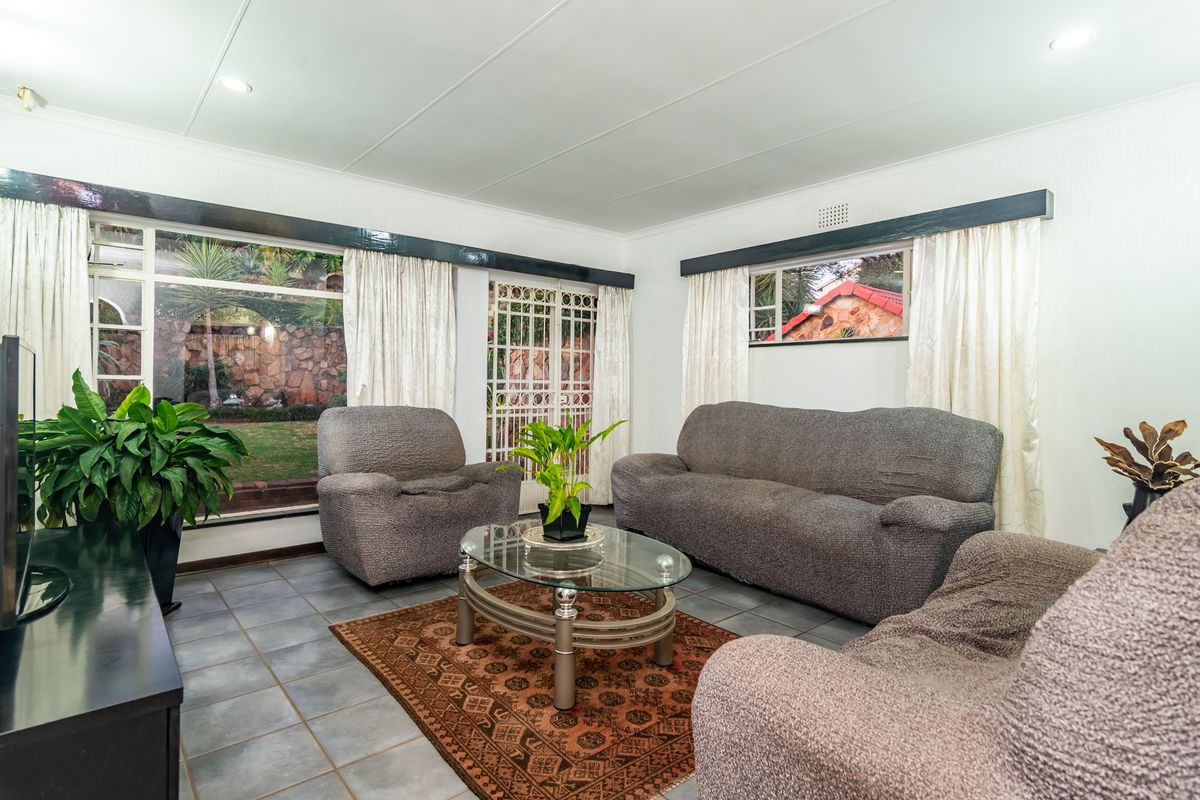 A bright living room featuring tiled flooring, large windows with garden views, and a security gate leading to the exterior.