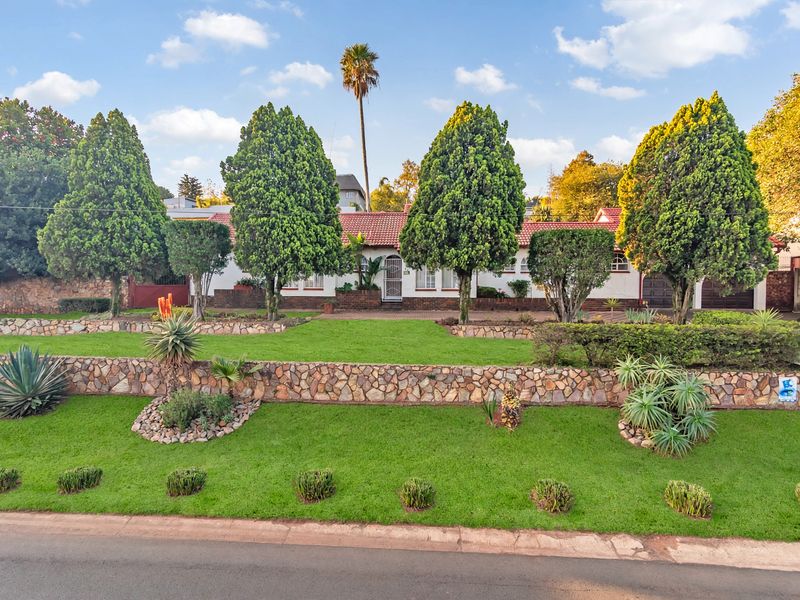 A well-maintained front elevation of a house featuring tiered stone retaining walls, a manicured lawn, mature landscaping, and a classic tiled roof.