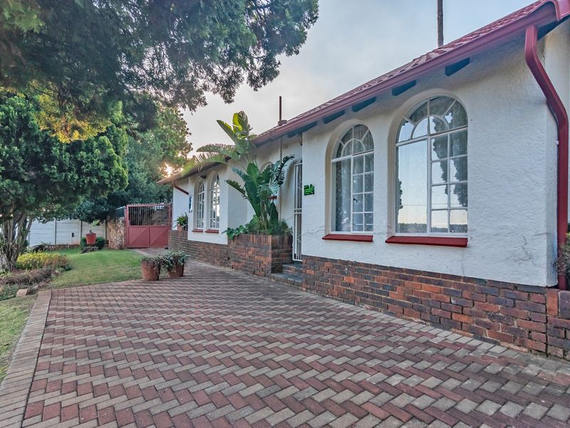 Rear exterior view of the house featuring a brick paved patio, arched windows, and a well-maintained garden area.