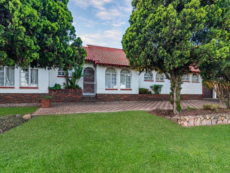 Front elevation of a charming house featuring a terracotta tile roof, arched windows, brick base detailing, and a well-maintained paved driveway and garden.