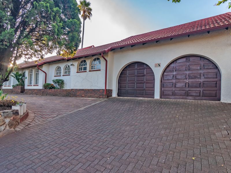Front elevation of a house featuring a double garage with arched doors, brick paved driveway, and classic arched windows under a tiled roof.