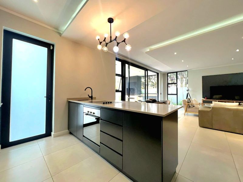 Modern open-plan living area featuring a sleek kitchen island with built-in appliances, tiled floors, and large sliding doors leading to the outdoor space.