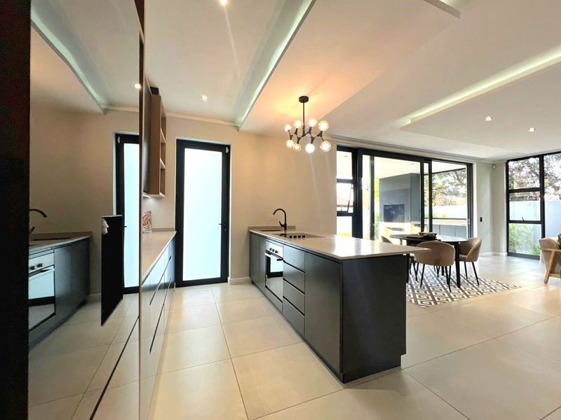 Modern open-plan kitchen and living area featuring a sleek island, built-in appliances, recessed lighting, and large sliding doors leading to the outdoor space.