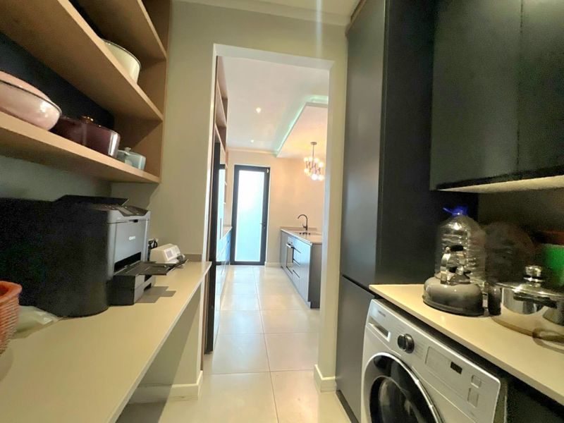 Modern scullery featuring sleek dark cabinetry, stone countertops, and tiled flooring, with a seamless transition into the adjacent kitchen area.