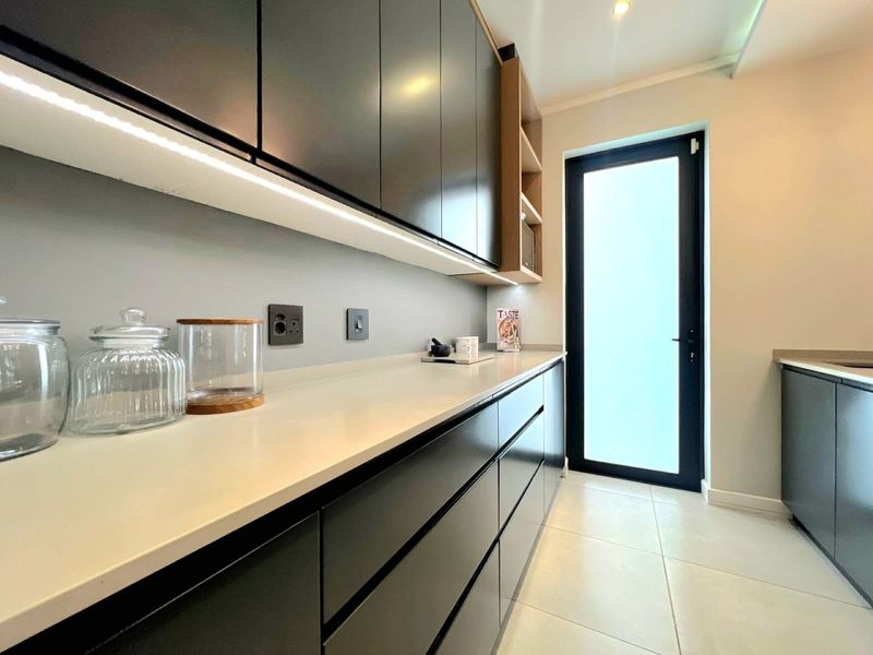 Modern scullery featuring sleek dark cabinetry, stone countertops, under-cabinet lighting, and tiled flooring, providing a clean and functional secondary prep area.