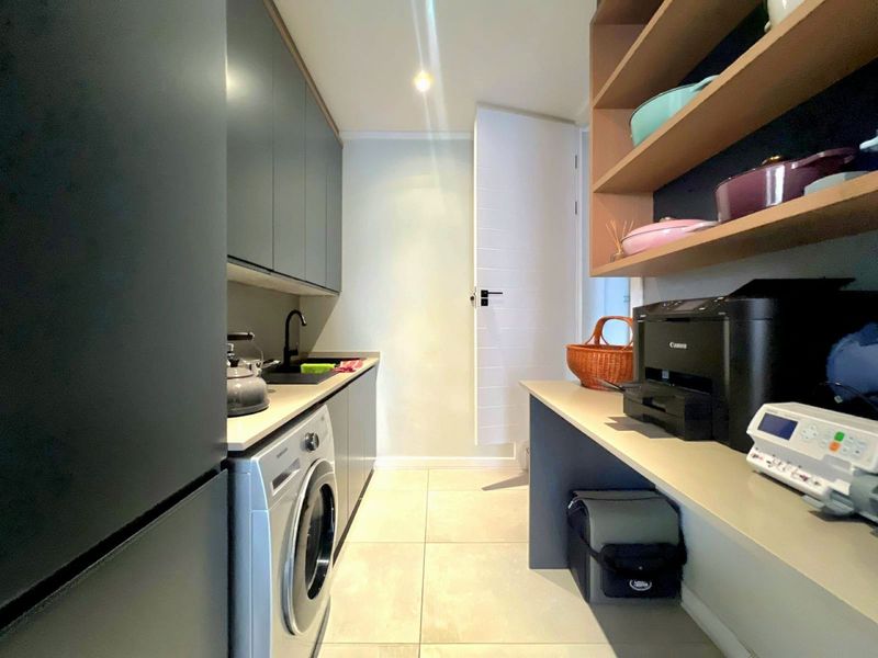 Modern laundry room featuring sleek dark cabinetry, integrated sink, tiled flooring, and ample open shelving for organized storage.
