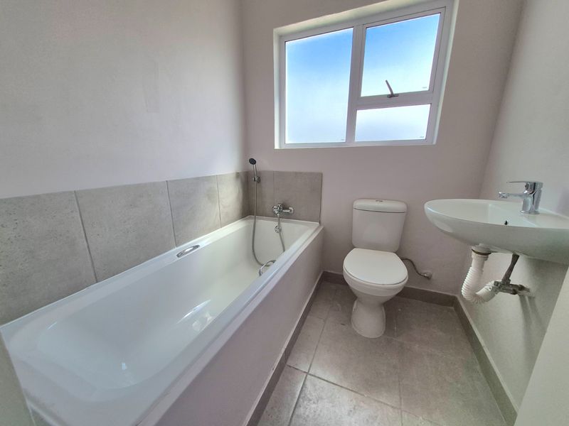 A functional bathroom featuring a bathtub with handheld shower, a toilet, and a wall-mounted basin with tiled flooring and splashback.