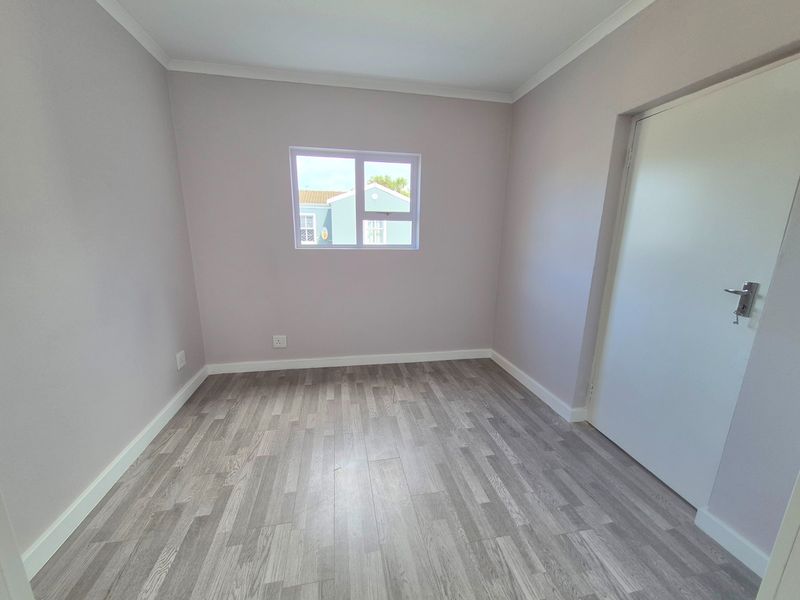 A clean, empty bedroom featuring modern grey laminate flooring, neutral wall paint, and crisp white trim, ready for personalization.