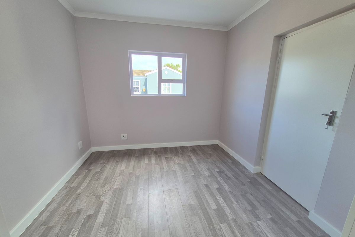 A clean, empty bedroom featuring modern grey laminate flooring, neutral wall paint, and crisp white trim, ready for personalization.