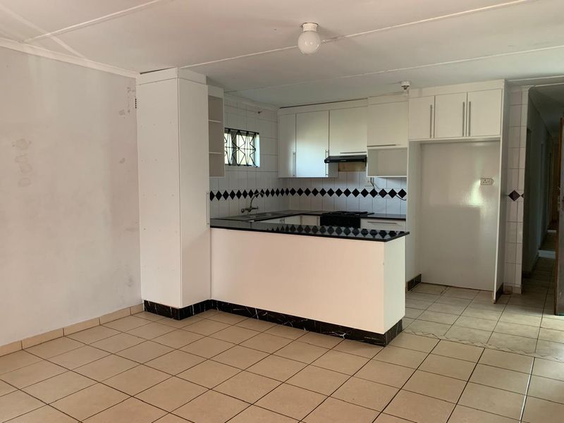 Open plan kitchen area featuring white cabinetry, black countertops, tiled backsplash, and ceramic flooring in a functional, vacant space.