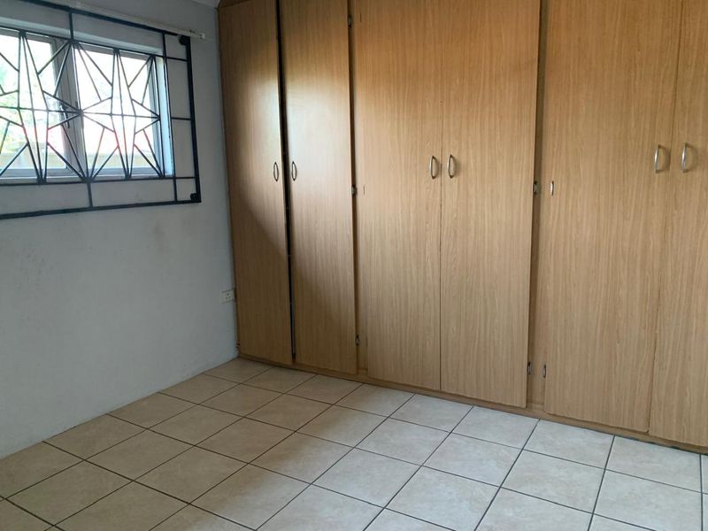 A functional bedroom featuring tiled flooring and extensive built-in wooden cupboards, providing ample storage space.