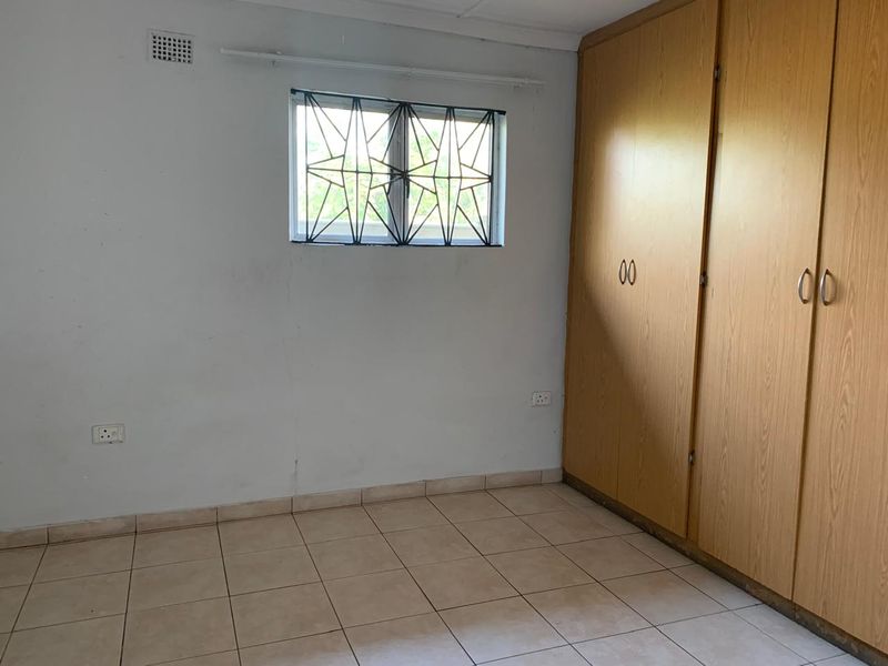 A vacant bedroom featuring tiled flooring, built-in wooden cupboards, and a window fitted with security bars.