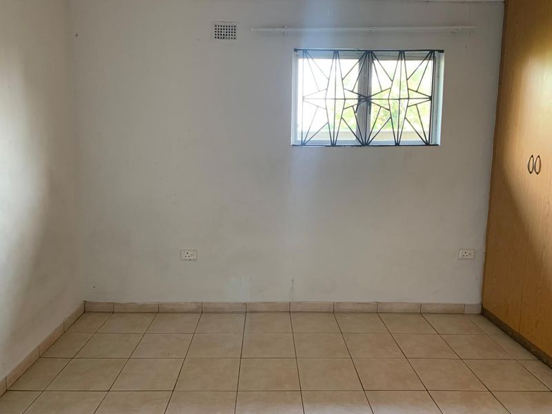 An empty bedroom featuring tiled flooring, a built-in wardrobe, and a window fitted with security bars.