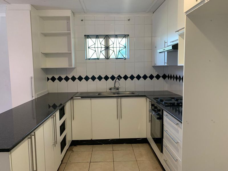A functional kitchen featuring white cabinetry, dark granite countertops, built-in oven and hob, and a tiled splashback with decorative accents.