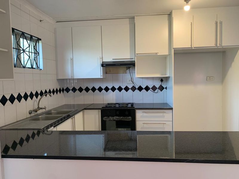 A functional kitchen featuring white cabinetry, dark granite countertops, a built-in oven, hob, and extractor fan with a tiled backsplash.