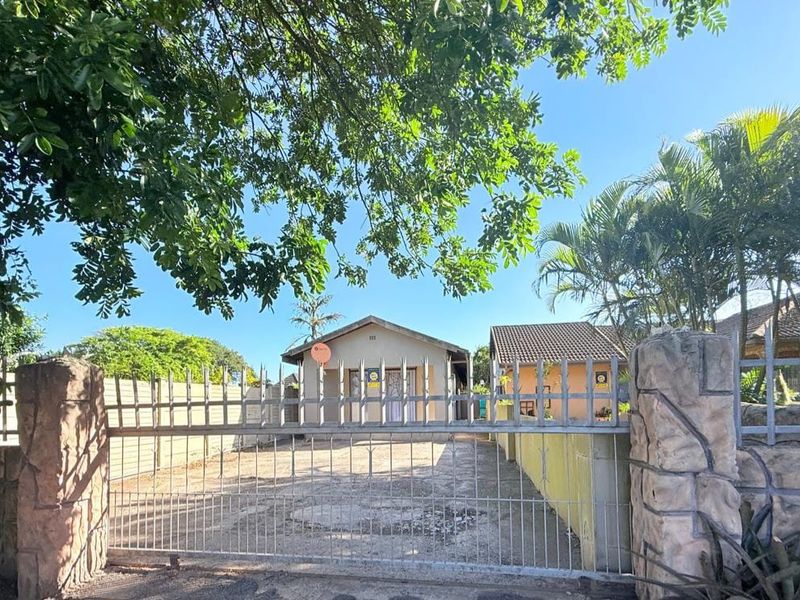 Front view of the cottage property featuring a gated entrance, concrete driveway, and perimeter walling with stone-clad pillars.