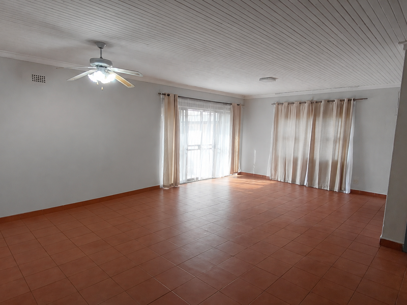A spacious, empty living room featuring tiled flooring, a ceiling fan, and a timber-look ceiling, offering a blank canvas for interior design.