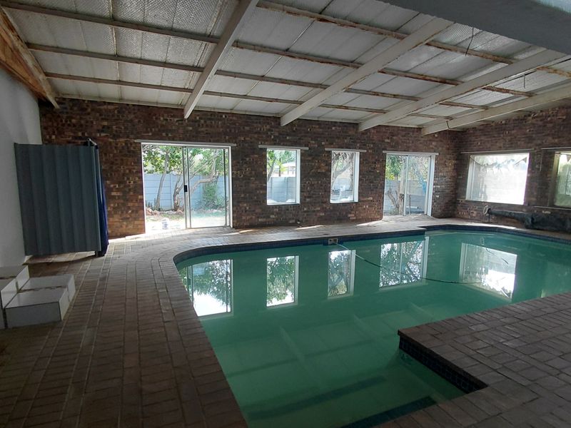 Spacious indoor swimming pool area featuring exposed brick walls, a high exposed beam ceiling, and large sliding glass doors leading to the garden.