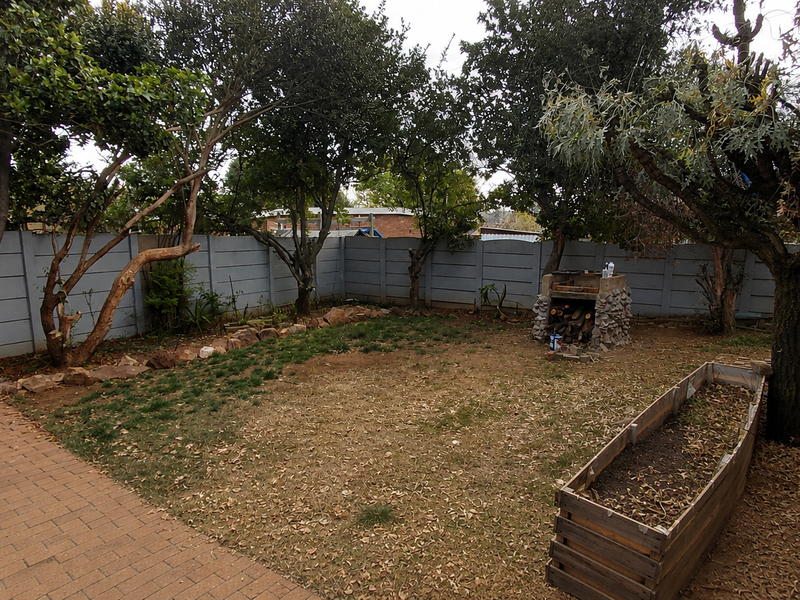 A private rear garden featuring a brick paved patio, a built-in braai, a raised planter box, and perimeter precast concrete walling.