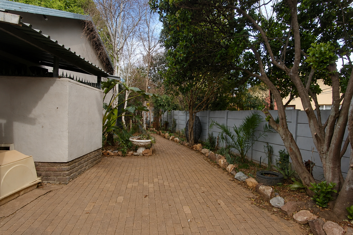 A paved side walkway leading to the rear garden, featuring mature trees and a secure precast concrete boundary wall.