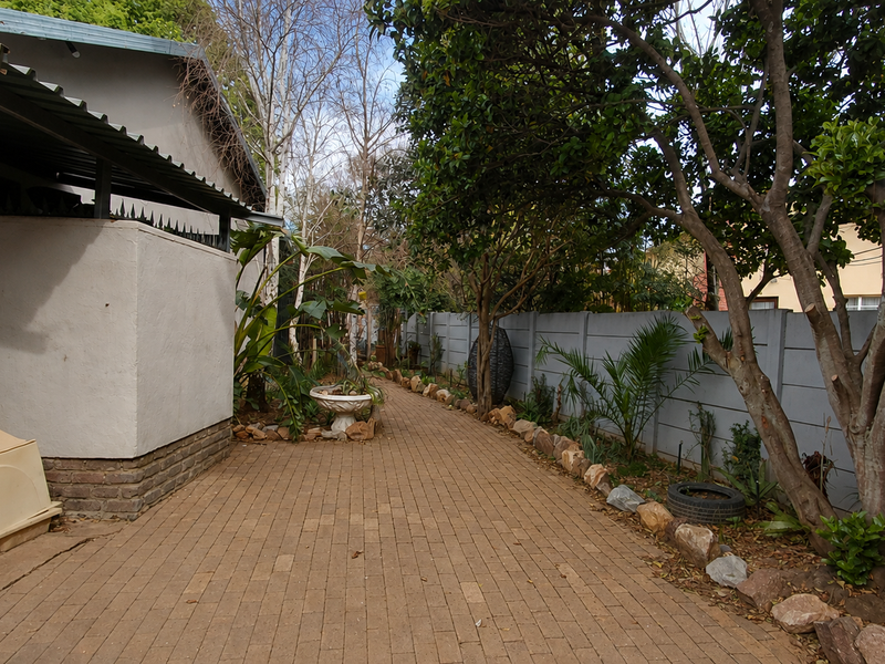 A paved side walkway leading to the rear garden, featuring mature trees and a secure precast concrete boundary wall.