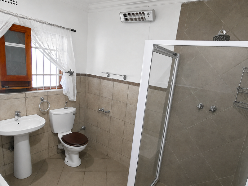 A functional bathroom featuring a pedestal basin, toilet, and a glass-enclosed shower with tiled finishes throughout.