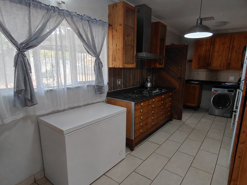 A functional kitchen featuring wooden cabinetry, a gas hob with extractor fan, and tiled flooring, offering a practical layout for daily meal preparation.