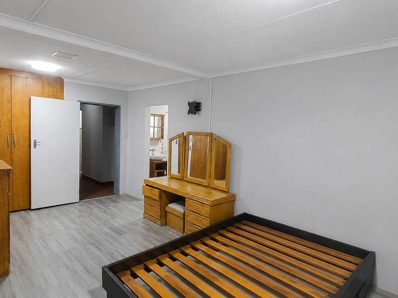 A spacious bedroom featuring built-in wooden cupboards, laminate flooring, and neutral wall finishes, with direct access to an adjoining room.
