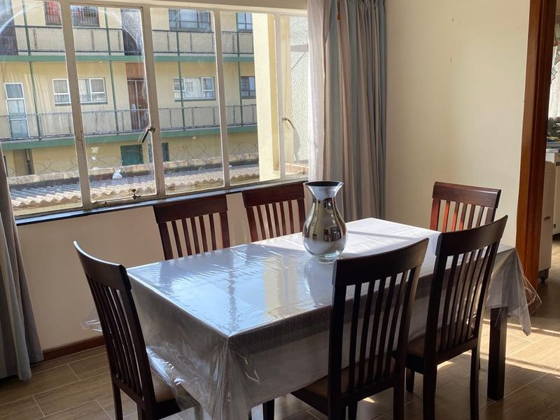 A dining room featuring tiled flooring, a ceiling fan, and a large window providing natural light and an urban view.
