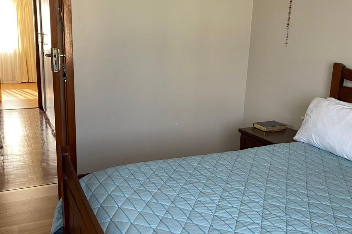 A bedroom featuring laminate flooring and a timber door frame, with a view into the adjacent hallway.