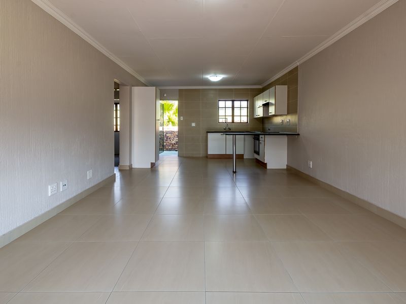 Spacious open-plan living and kitchen area featuring neutral tiled flooring, built-in cabinetry, and a functional kitchen layout with integrated appliances.