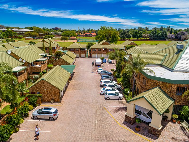 Aerial view of a residential complex featuring brick buildings with green tiled roofs, paved driveways, and ample parking space within a landscaped estate.