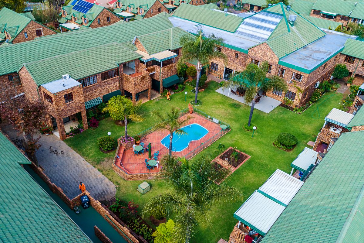 Aerial view of a residential complex featuring a central communal garden, swimming pool, paved patio areas, and brick buildings with green tiled roofs.